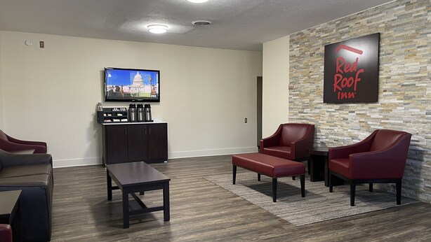 Eine Hotelhalle mit Steinwand, einem Red Roof Inn Schild, einem Fernseher, einer Kaffeestation und Ledersesseln.