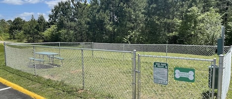 A fenced dog park with a picnic table and a sign indicating rules.