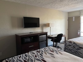 Una habitación de hotel con cama, escritorio, televisor, lámpara y armario.