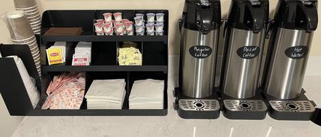A coffee station with a coffee machine, a water dispenser, and a shelf with coffee pods and napkins.