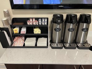 A coffee station with a coffee machine, a water dispenser, and a shelf with coffee pods and napkins. - Red Roof Inn LaGrange (LaGrange)