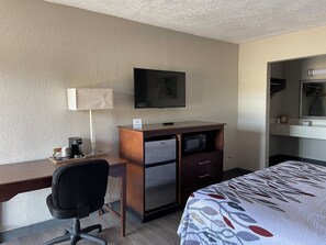 Ein Hotelzimmer mit Schreibtisch, Stuhl, Bett, Fernseher, Kühlschrank und Mikrowelle.