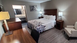 Una habitación de hotel con cama, mesitas de noche, un escritorio, una silla y una obra de arte en la pared.