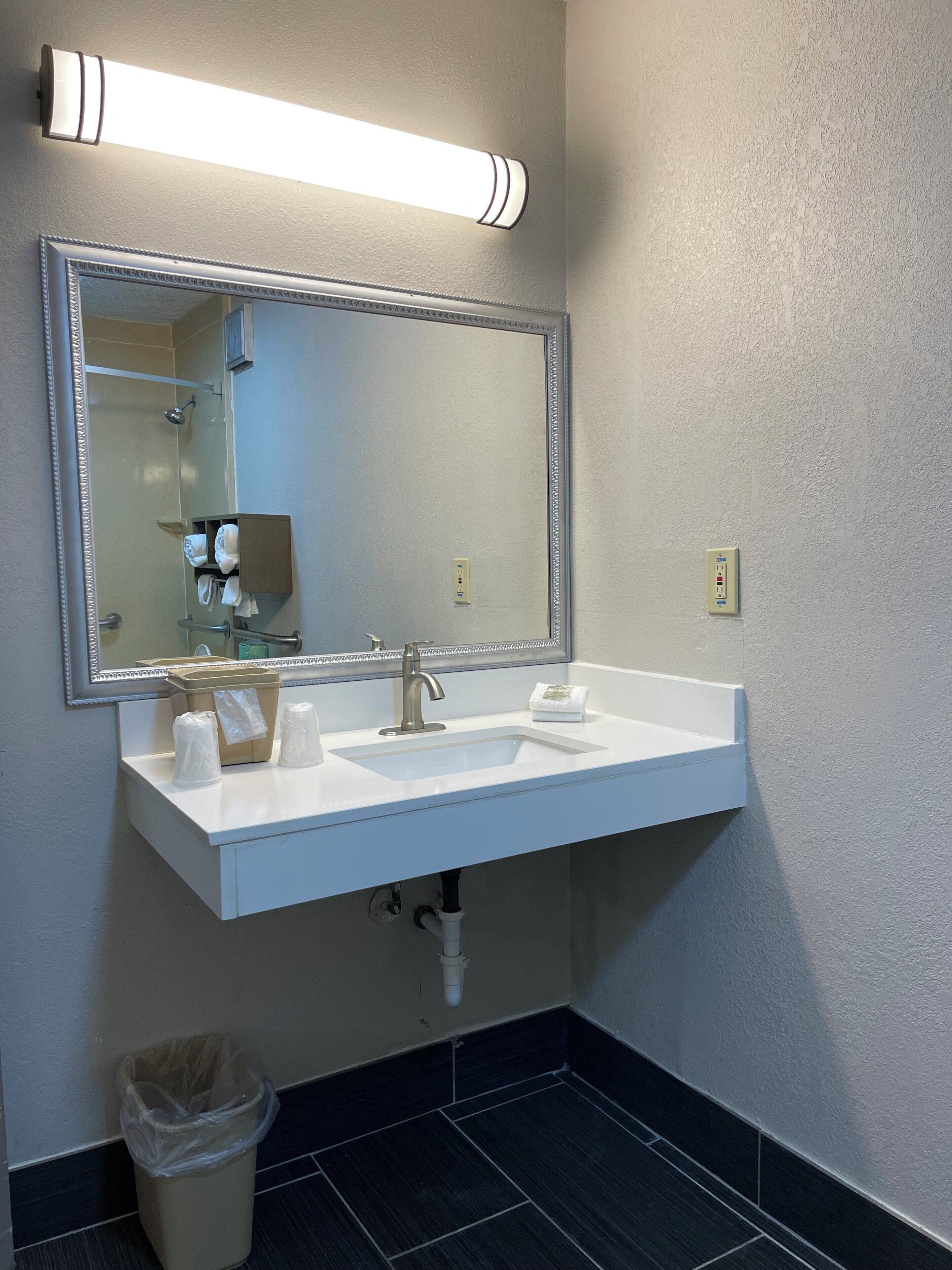 A bathroom with a white sink, a mirror, a towel dispenser, and a trash can.