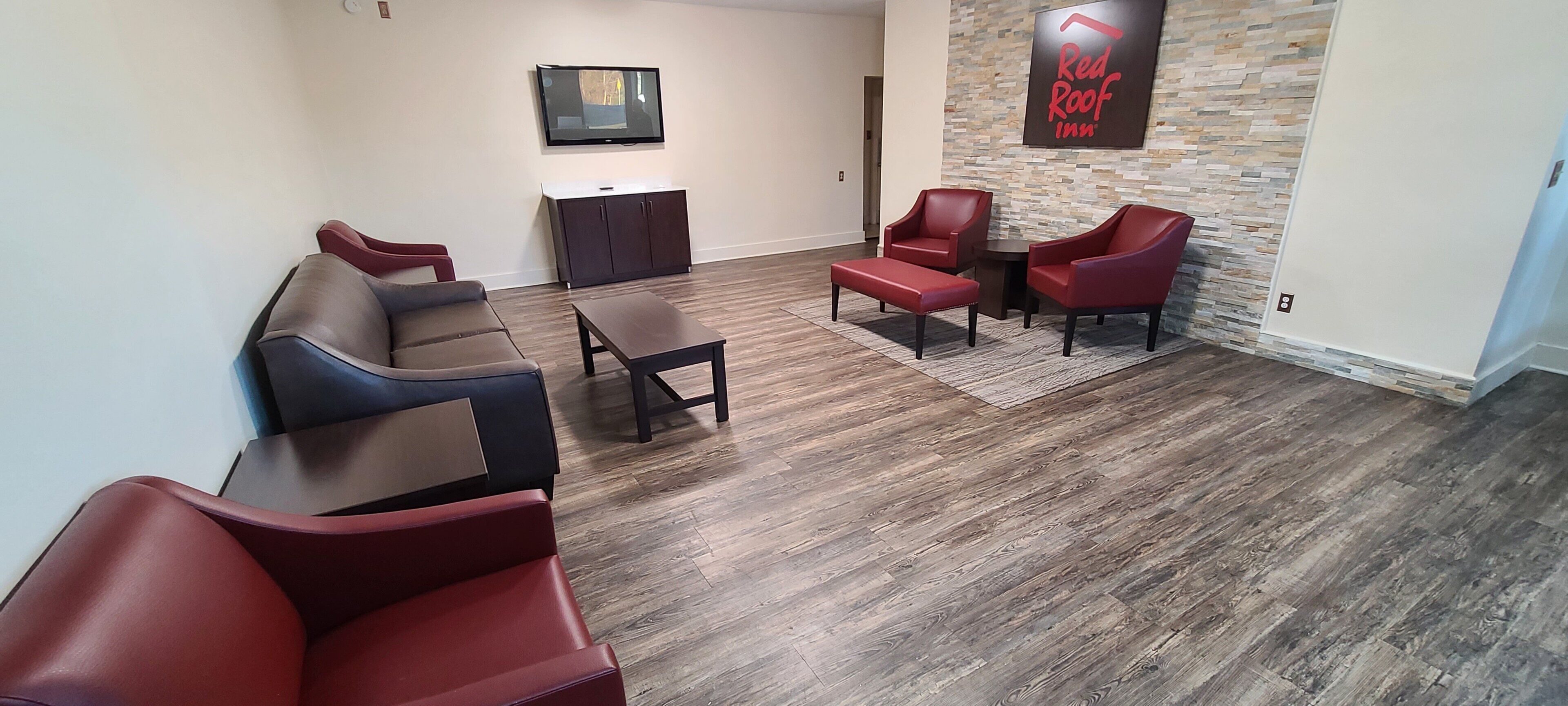 Een hotel lobby met lederen zitplaatsen, een flatscreen televisie en een Red Roof Inn bord.