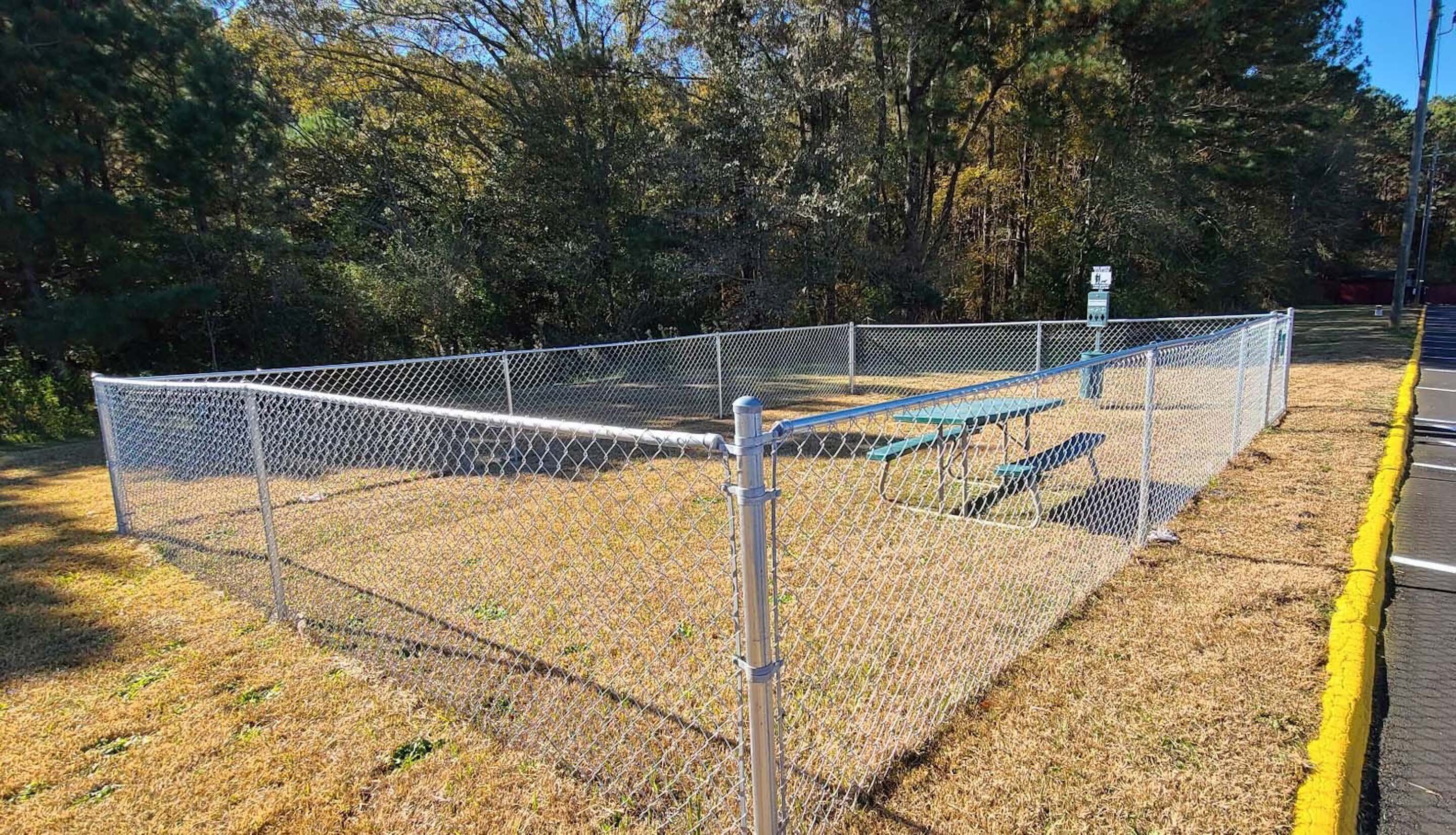 A fenced area with a metal gate, a picnic table, and a bench.