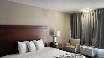A hotel room with a large bed, a bedside table, a lamp, a chair, and a window with curtains.