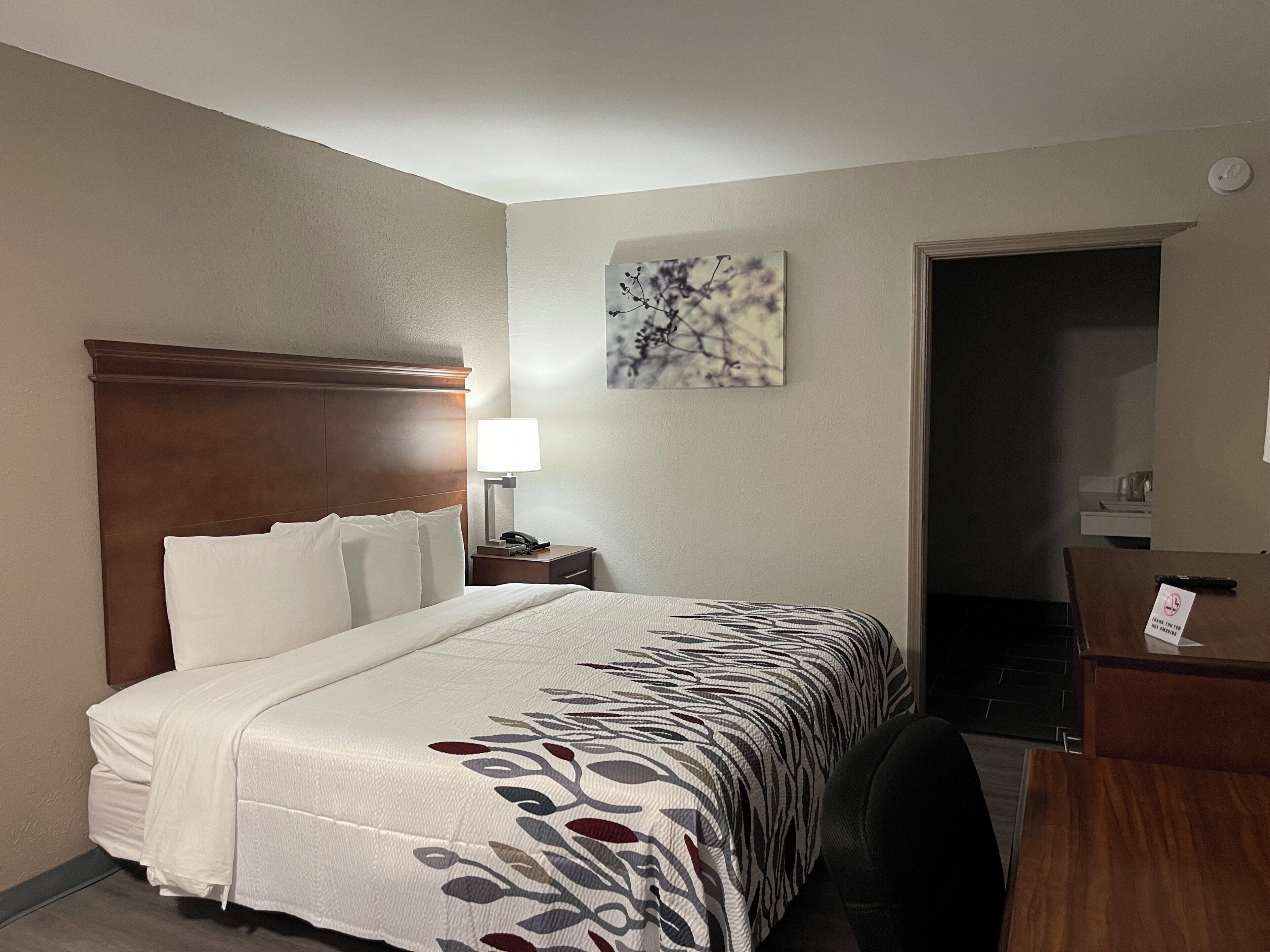 Una habitación de hotel con cama, mesita de noche, lámpara, escritorio y silla.