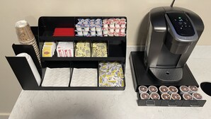 Eine Kaffeestation mit einer Kaffeemaschine, verschiedenen Kaffeekapseln und einer Auswahl an Servietten.