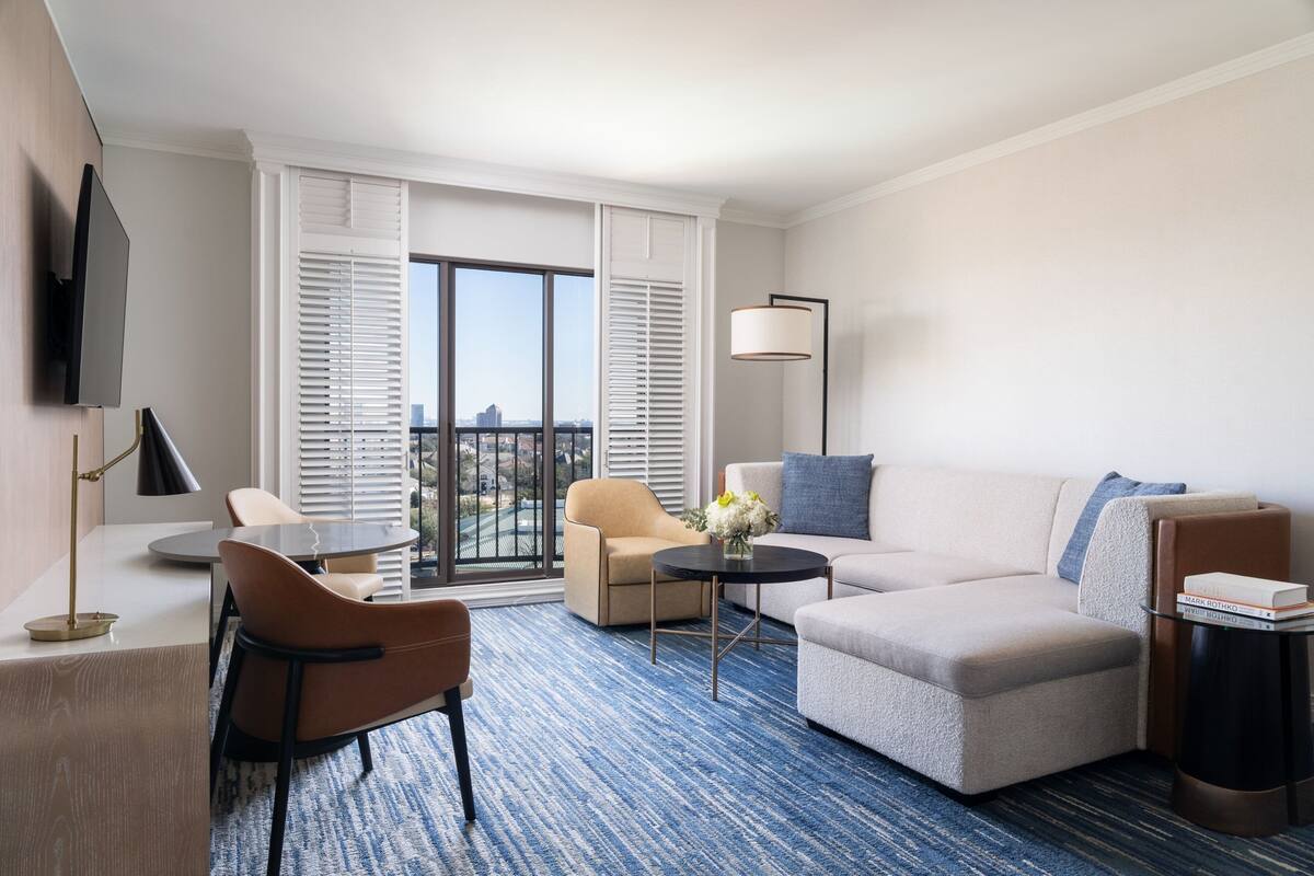 Una habitación de hotel moderna con sofá, sillón, mesa de centro y televisión montada en la pared.