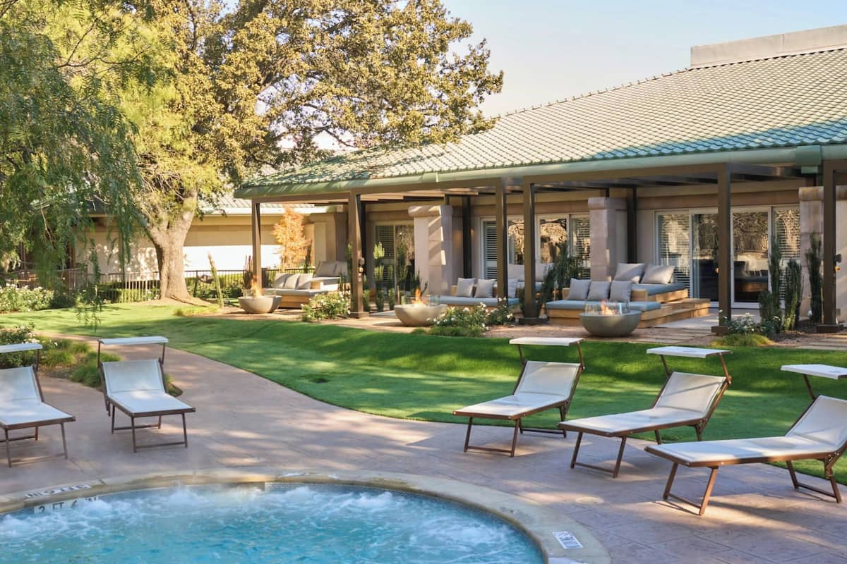 Zona de piscina con sillones reclinables, jacuzzi y un área de estar cubierta con mobiliario exterior.