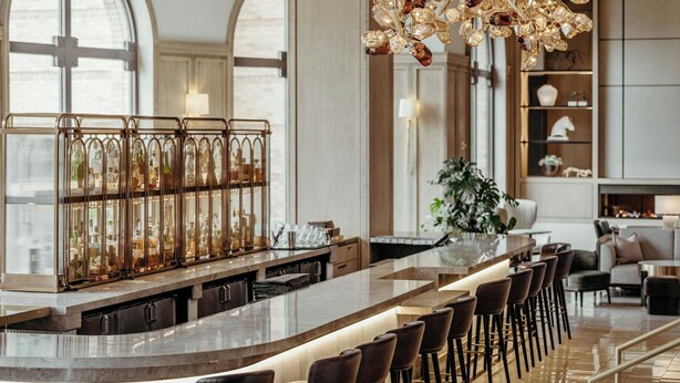 Un área de bar moderna con una barra alargada, varios taburetes y una lámpara decorativa.