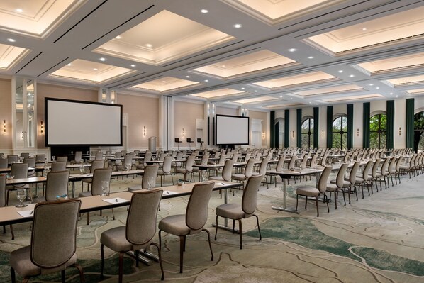 Une salle de conférence avec des rangées de tables et de chaises, de grands écrans et un sol recouvert de moquette.