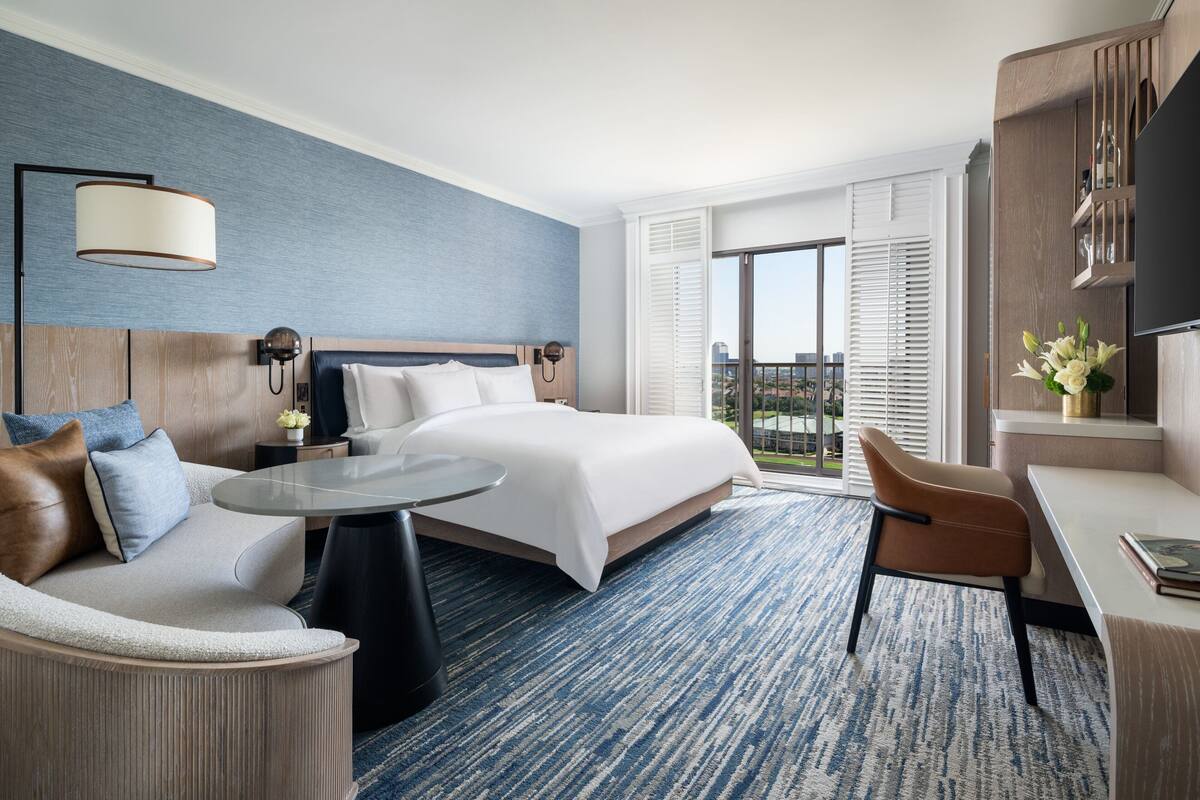 Habitación de hotel con una cama grande, un sofá, un escritorio y un balcón con vistas.