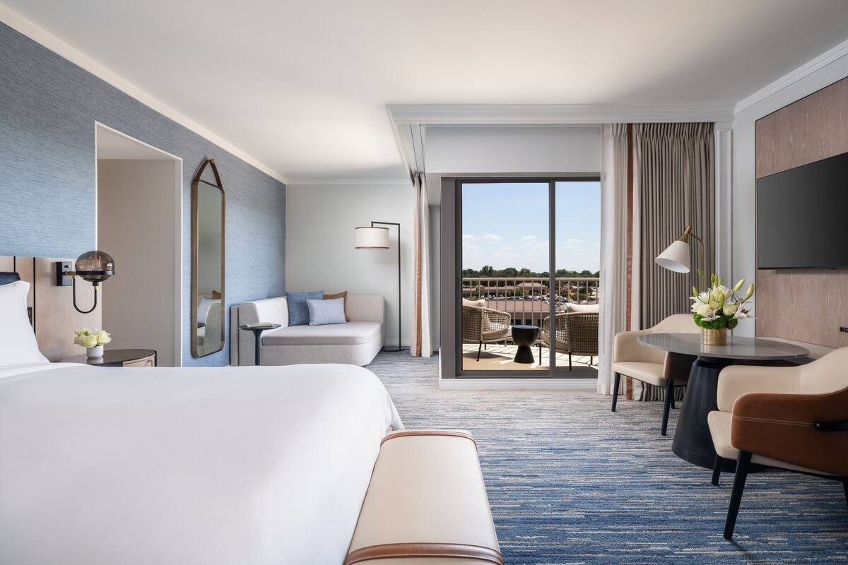 Habitación de hotel con una cama grande, un sofá, una mesa de comedor y vistas al exterior.