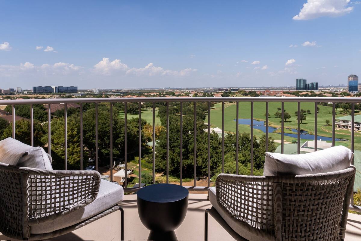Un balcón con mobiliario de mimbre, una mesa redonda y vistas a un campo de golf y al paisaje urbano.