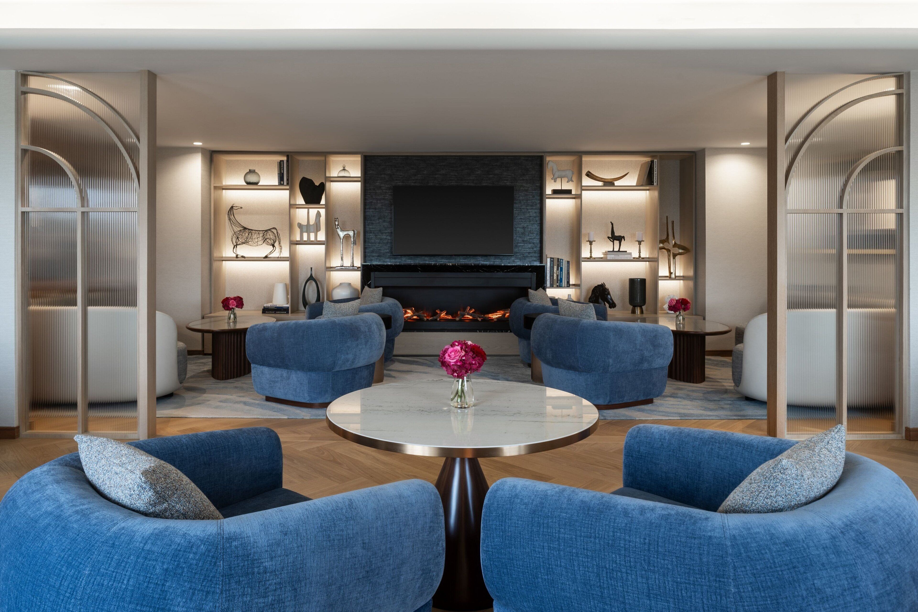 A modern living room with a fireplace, blue sofas, a round coffee table, and decorative items on shelves.