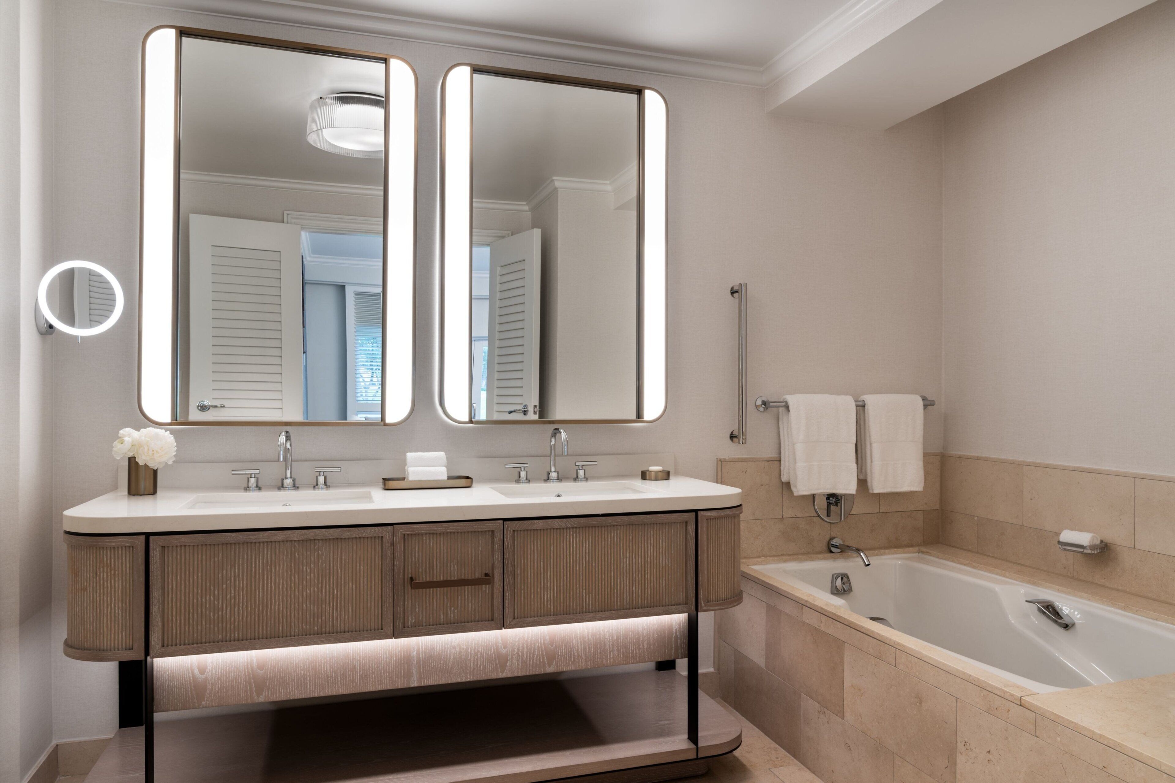 A modern bathroom with a double vanity, two mirrors, a bathtub, and a handrail.