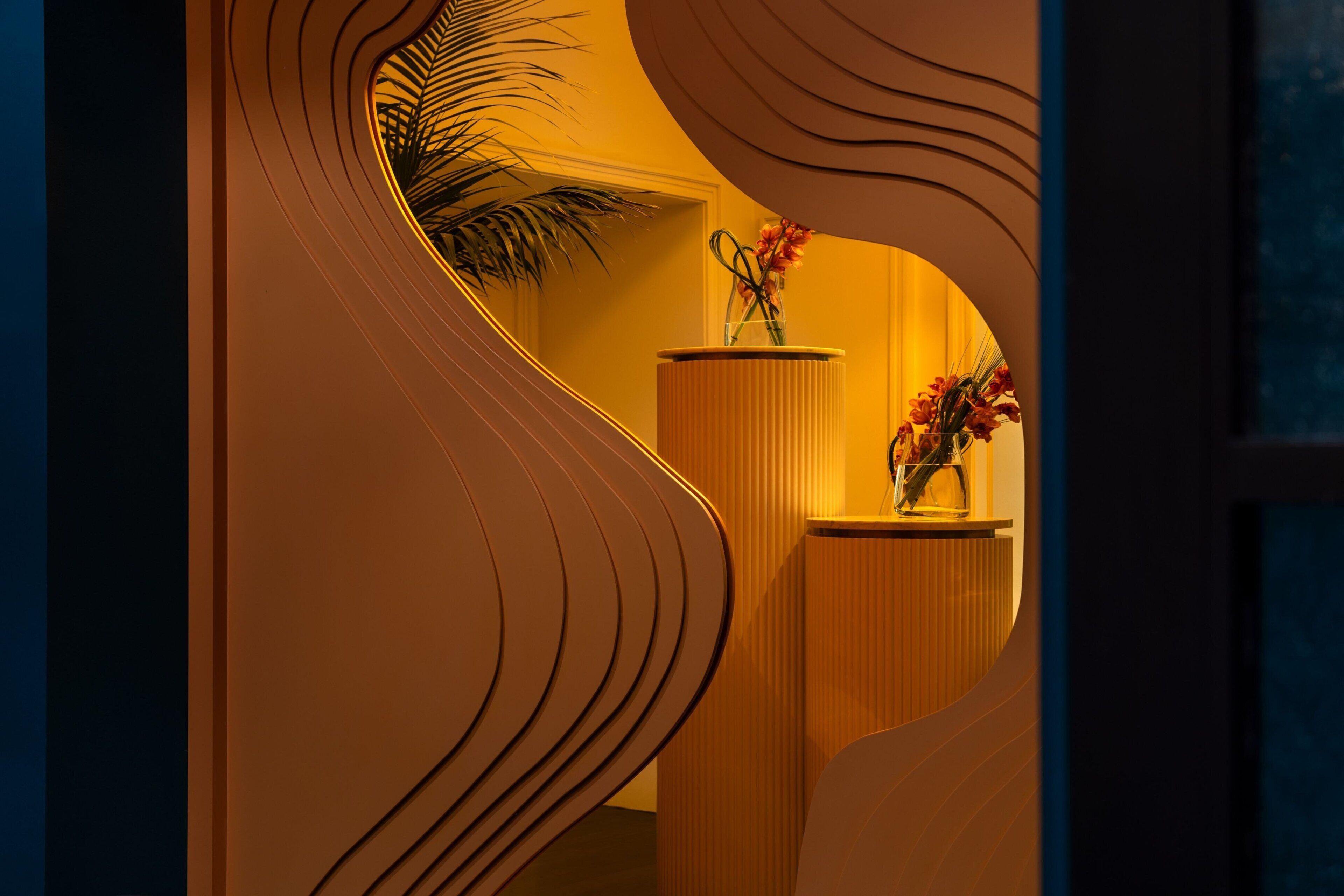 A modern interior with a curved wall design, a wooden reception desk, and a vase with flowers.