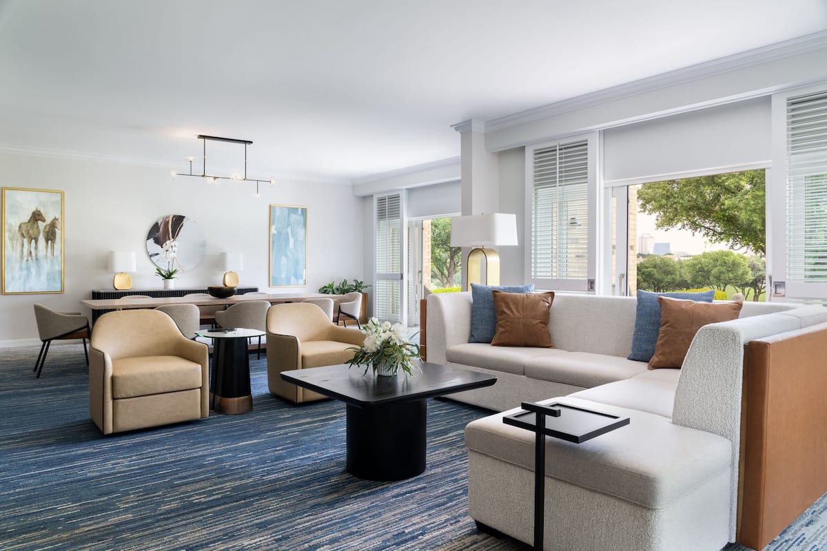 Una habitación de hotel moderna con zona de estar, comedor y ventanas amplias con vistas al exterior.