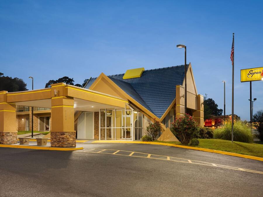Un hotel Super 8 con entrada cubierta, zona de estar exterior y cielo azul despejado.