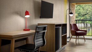 A modern room with a wooden desk, a black office chair, a red desk lamp, a black TV, and a red chair.