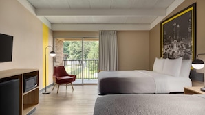 A hotel room with a bed, a desk, a chair, a TV, and a window with a view of greenery.