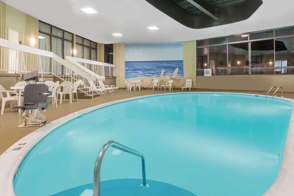 Una piscina interior con vistas al océano a través de amplios ventanales, rodeada de sillones blancos y una tumbona.