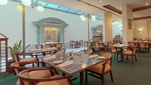 En restaurant med flere spiseborde, møbleret med træ og med grønt tæppe på gulvet.