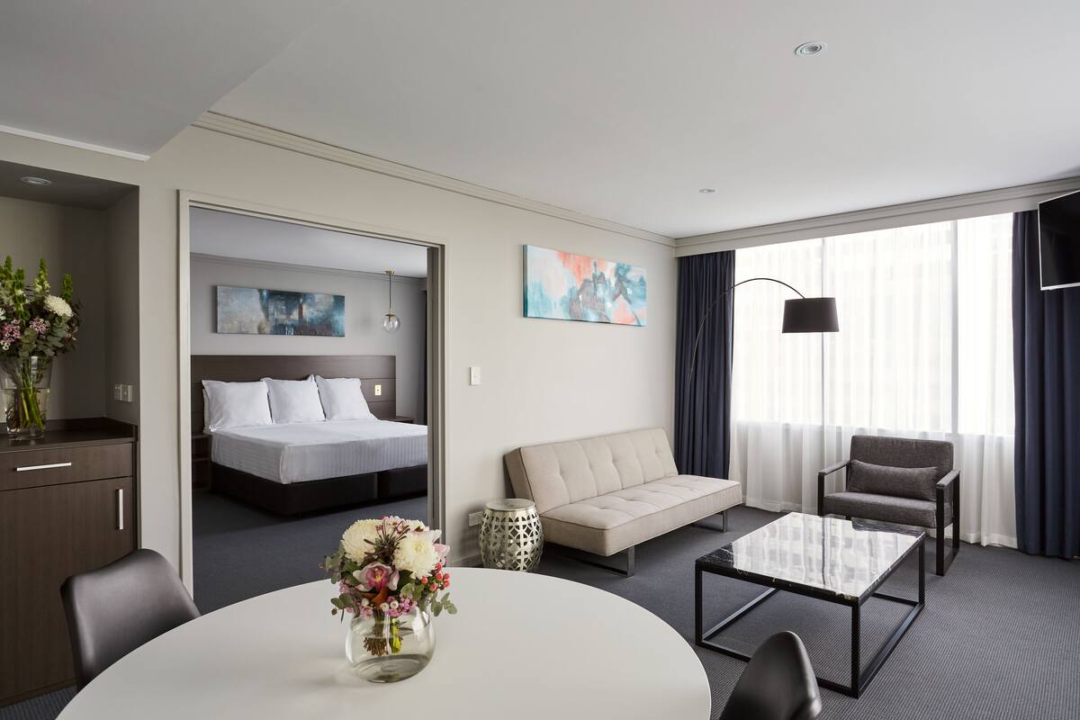 Quarto de hotel com cama, sofá, mesa de centro e mesa de jantar.