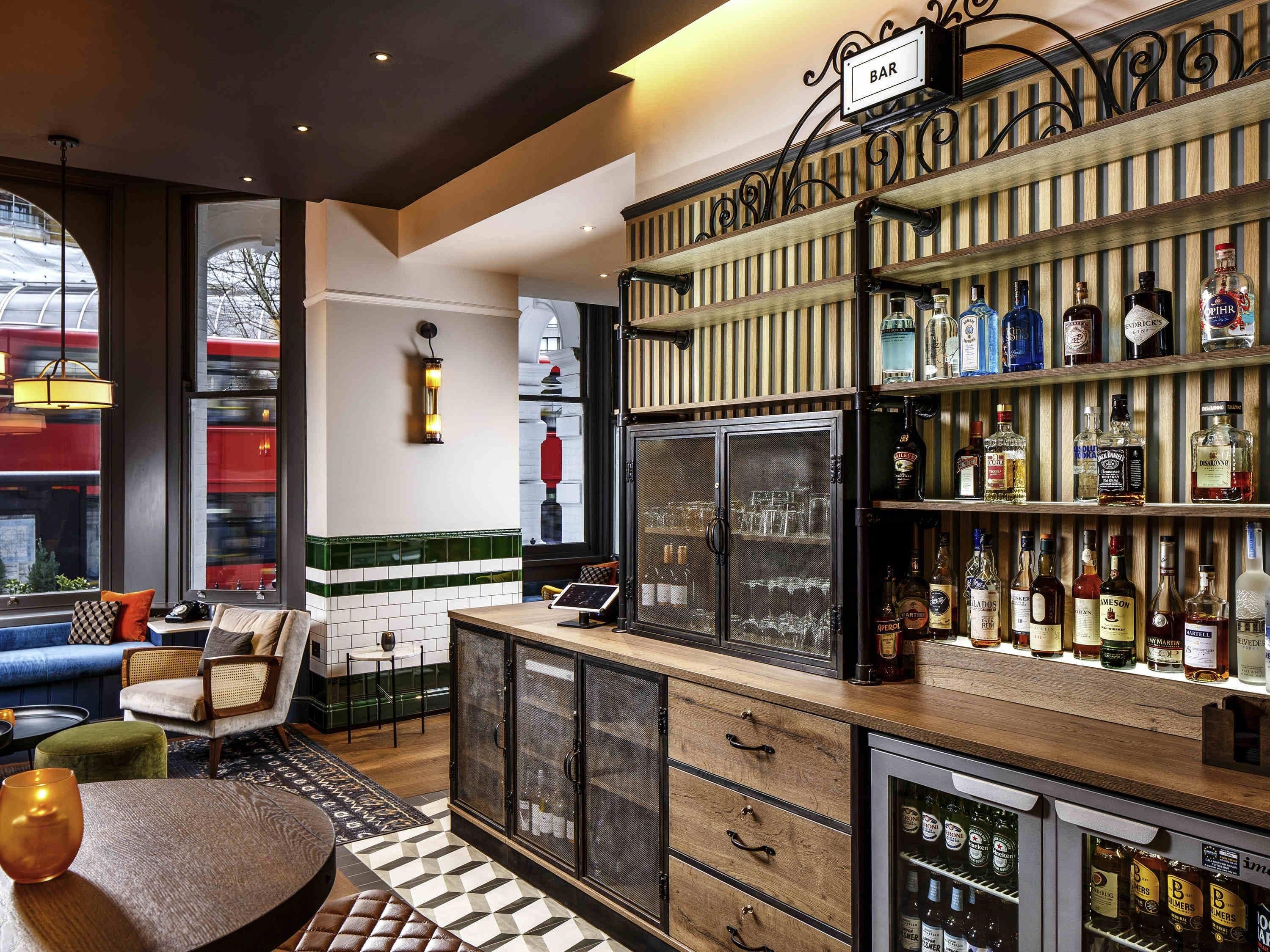 A bar area with a variety of liquor bottles, a refrigerator, and a seating area with a view of a train outside.