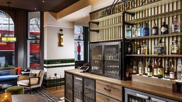 A bar area with a variety of liquor bottles, a refrigerator, and a seating area with a view of a train outside.