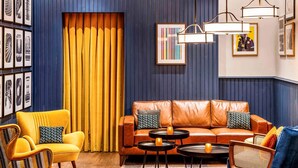 A room with a leather sofa, yellow armchairs, and a blue armchair, with a patterned rug and framed pictures on the walls. - ibis Styles London Gloucester Road (London)
