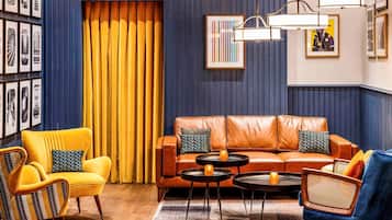 A room with a leather sofa, yellow armchairs, and a blue armchair, with a patterned rug and framed pictures on the walls.