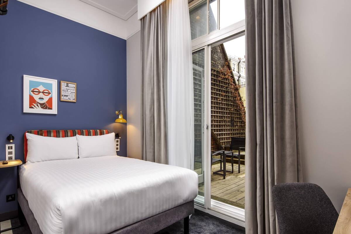 A hotel room with a bed, a desk, a chair, and a view of the outside.