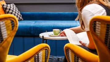A person sitting on a blue couch with a book and a cup on a small table.