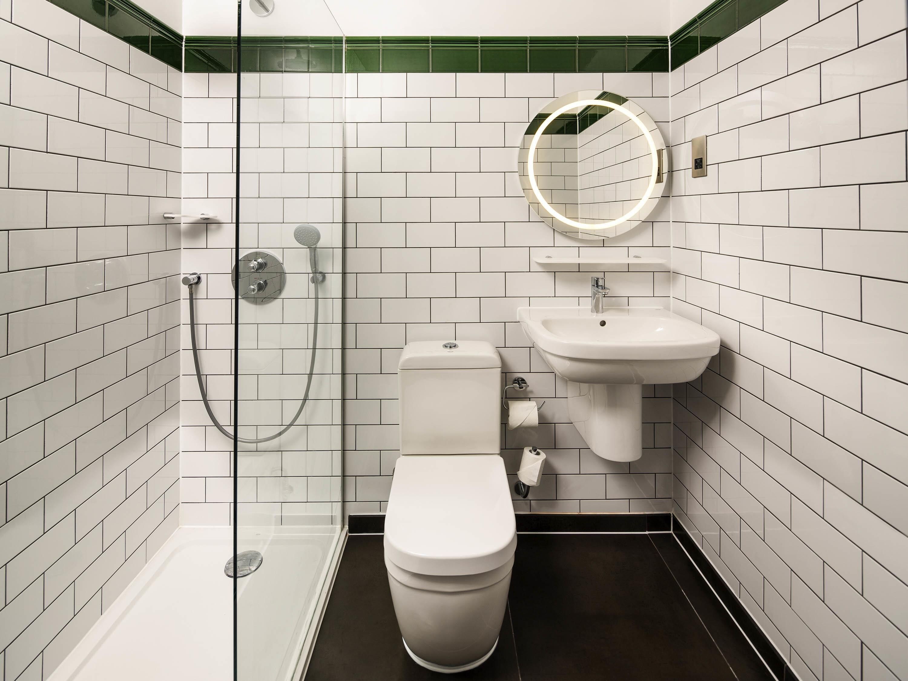 Une salle de bain moderne avec une douche à parois de verre, des toilettes blanches, un lavabo avec un miroir et des murs recouverts de carreaux blancs.