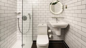 Une salle de bain moderne avec une douche à parois de verre, des toilettes blanches, un lavabo avec un miroir et des murs recouverts de carreaux blancs.