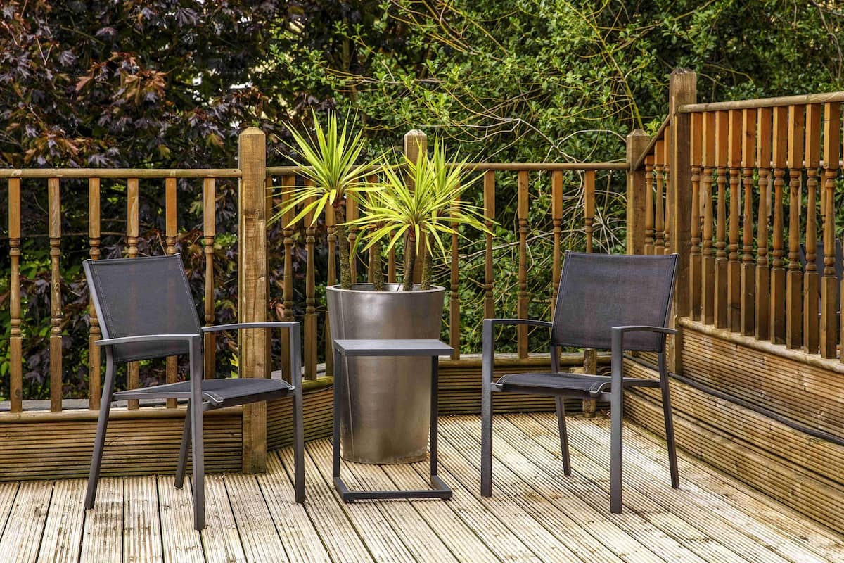 Una terraza de madera con dos sillas y una planta en maceta.