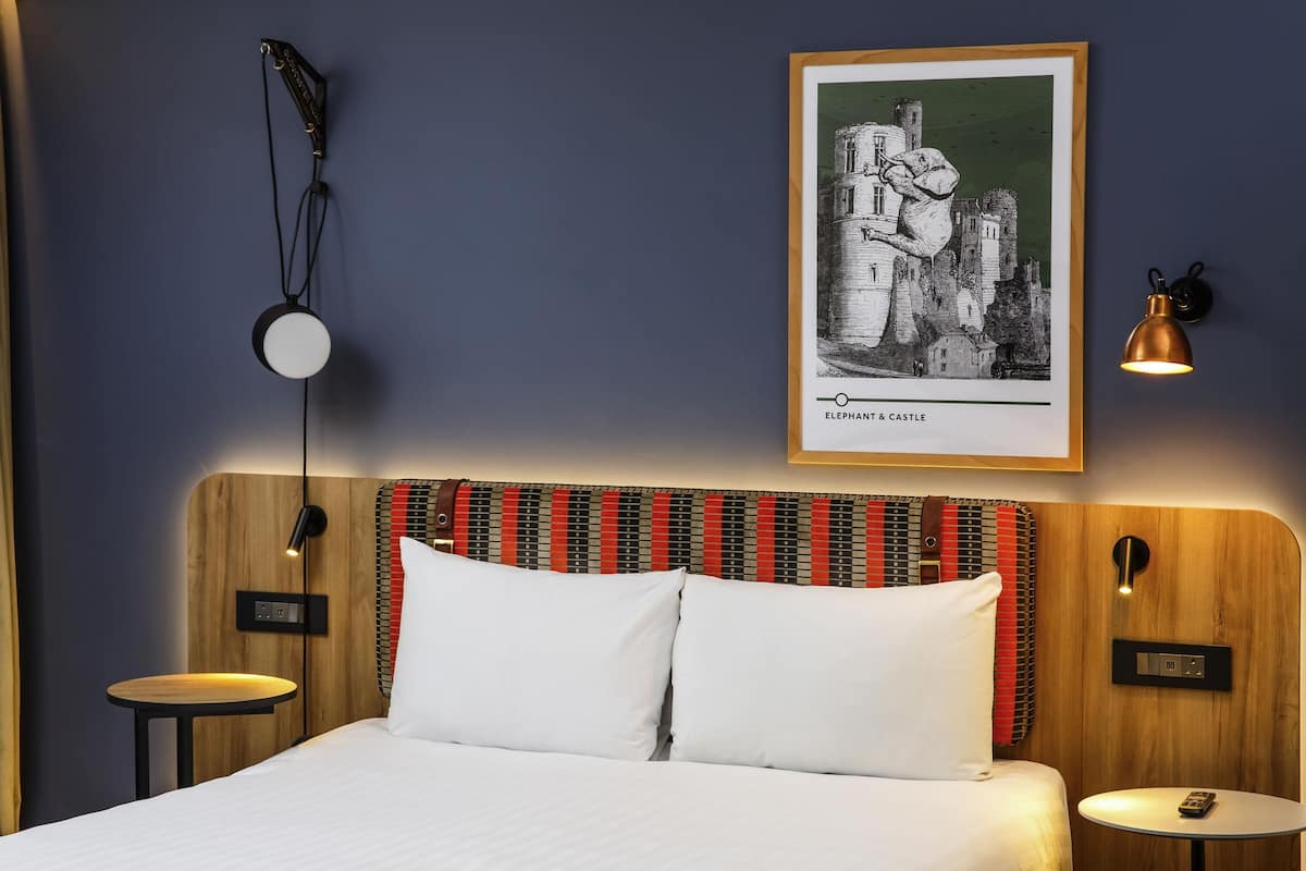 A hotel room with a bed, two bedside tables, a wall-mounted lamp, and a framed picture of an elephant and castle.