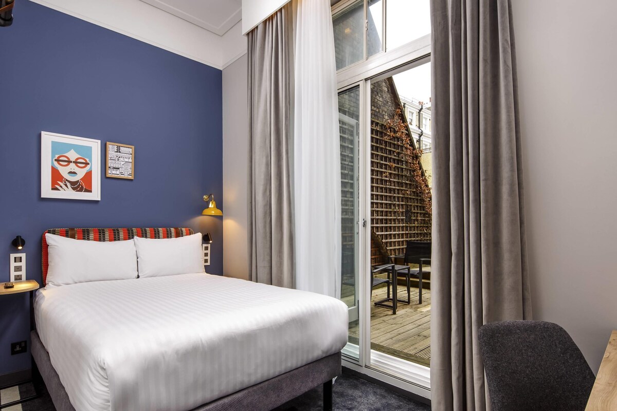 A hotel room with a bed, a desk, a chair, and a view of the outside.