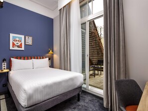 A hotel room with a bed, a desk, a chair, and a view of the outside. - ibis Styles London Gloucester Road (London)