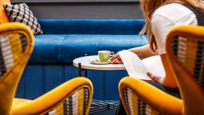 A person sitting on a blue couch with a book and a cup on a small table. - ibis Styles London Gloucester Road (London)