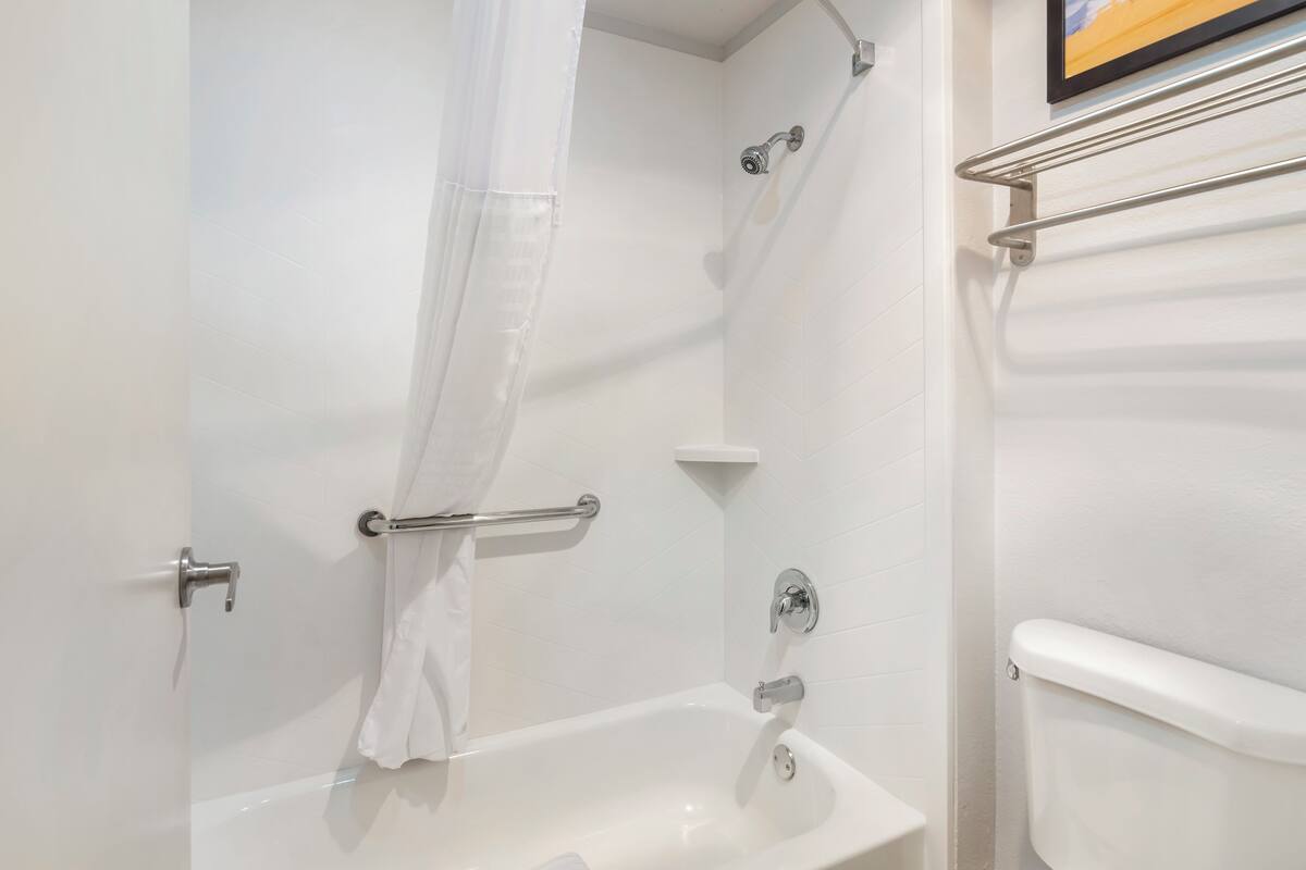 A bathroom with a white bathtub, a shower curtain, a towel rack, and a toilet.