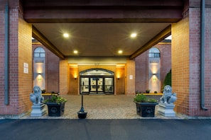 A hotel entrance with a brick facade, a glass door entrance, and two lion statues on either side.