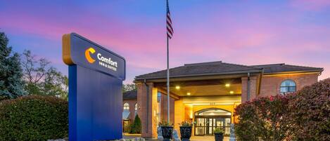 A hotel entrance with a sign, American flag, and a well-maintained lawn.
