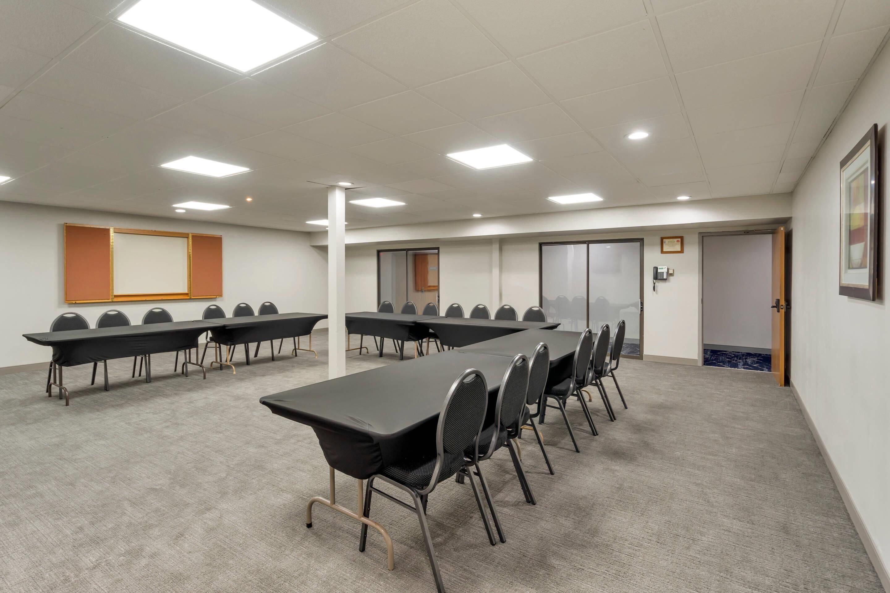 A conference room with multiple tables and chairs, white walls, and ceiling lights.