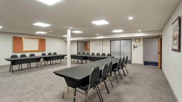 A conference room with multiple tables and chairs, white walls, and ceiling lights.
