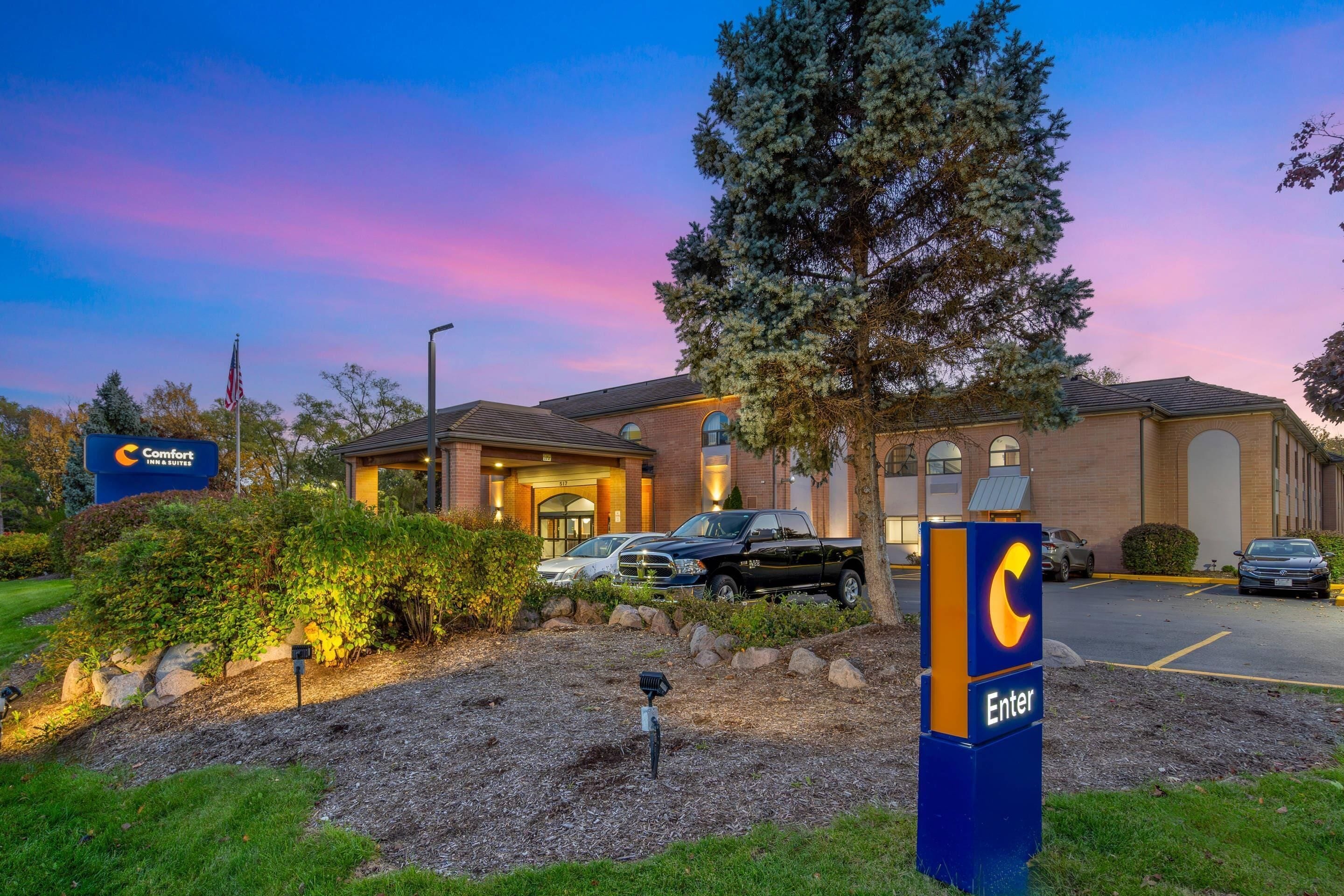 A hotel with a large parking lot, a sign with a 'C' logo, and a building entrance.