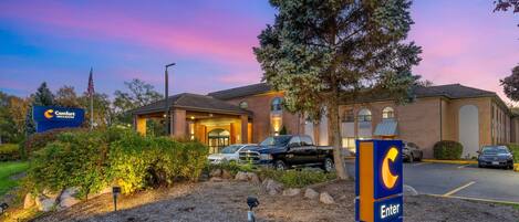 A hotel with a large parking lot, a sign with a 'C' logo, and a building entrance.